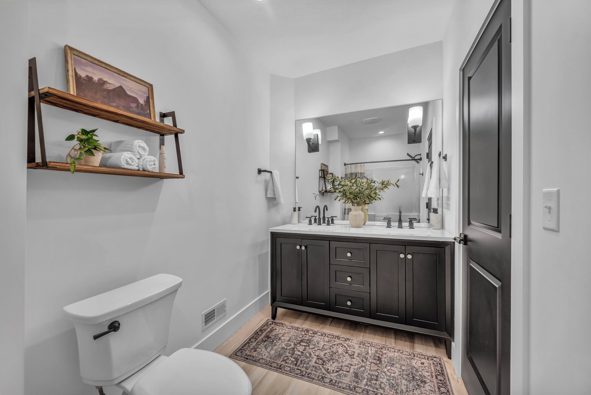 A modern bathroom with a toilet, dark wooden vanity, white sink, and a mirror.