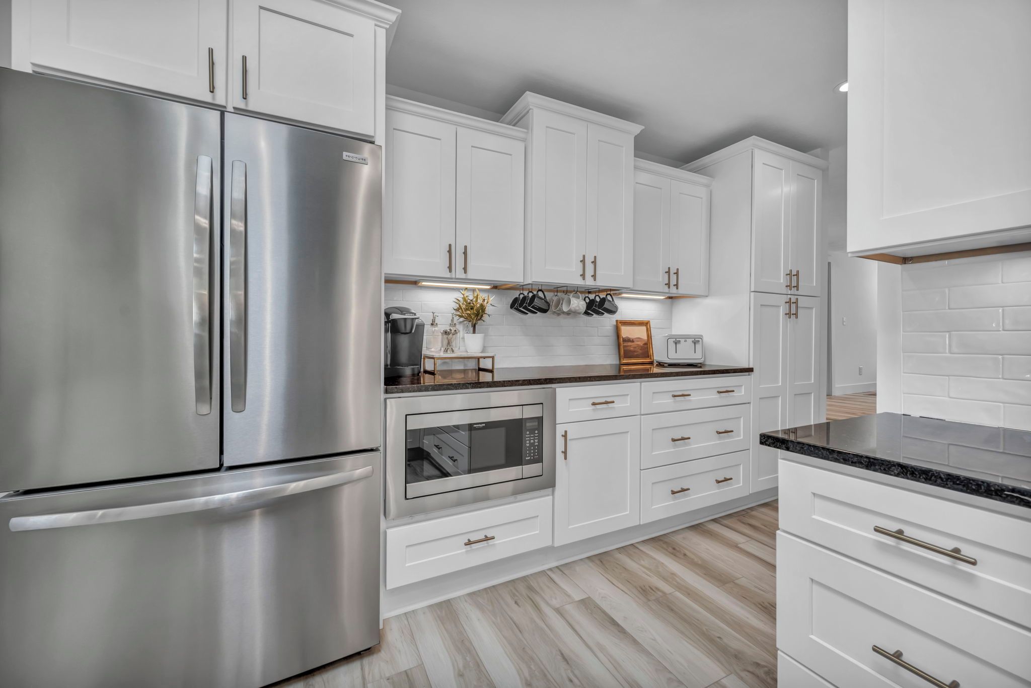 Une cuisine moderne avec des meubles blancs, des appareils en acier inoxydable et un plancher en bois.
