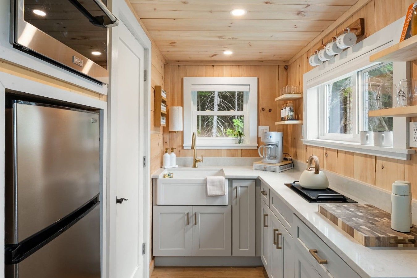 Una cocina compacta con un refrigerador de acero inoxidable, una cafetera y una tetera sobre la encimera.
