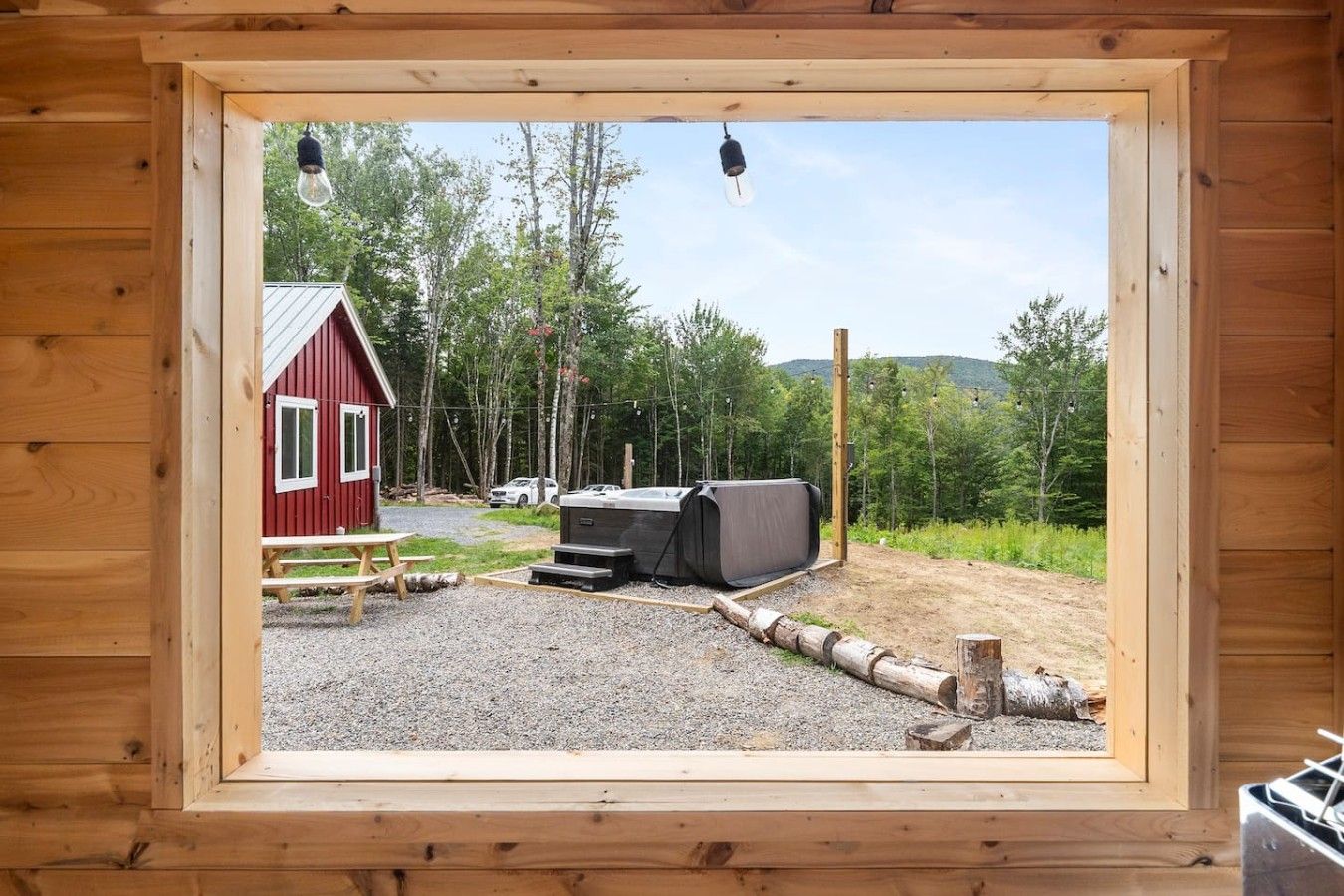 Una cabaña de madera con fachada roja, una mesa de picnic, un jacuzzi y un área de grava.