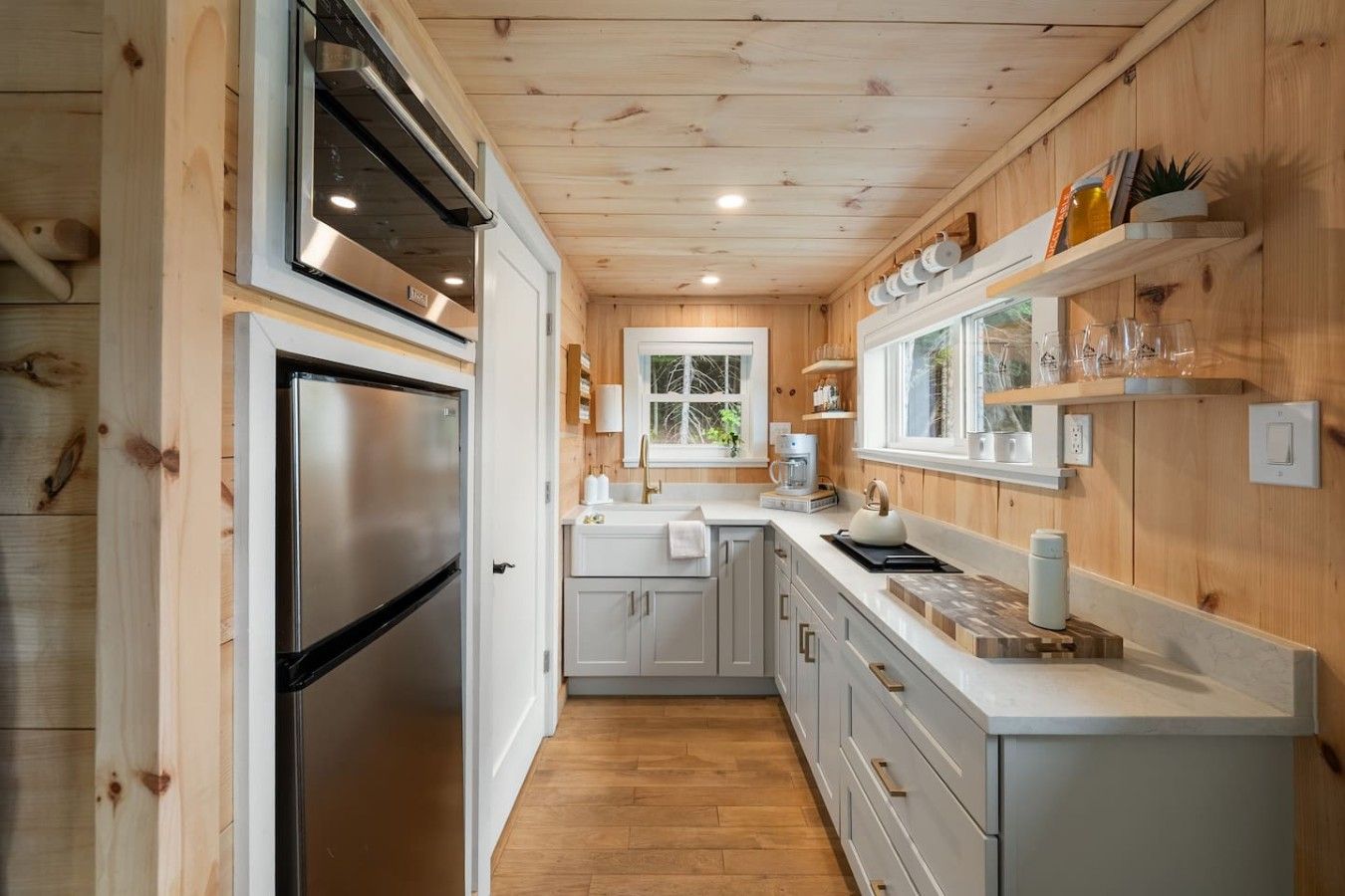 A modern kitchen with wooden walls, a stainless steel refrigerator, and a window overlooking greenery.