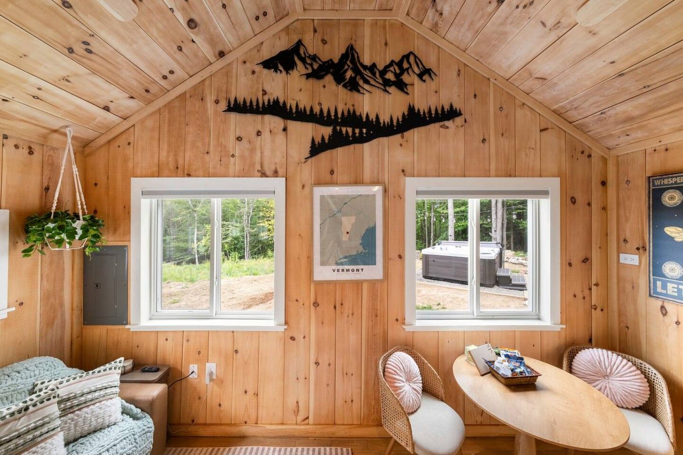 Interior de una cabaña con paredes de madera, dos ventanas, un mapa, un jacuzzi y una zona de estar acogedora.