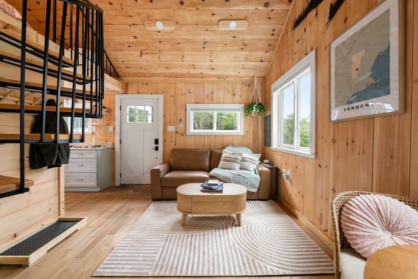 A cozy cabin interior with a wooden interior, a sofa, a coffee table, a hanging plant, and a framed map on the wall.