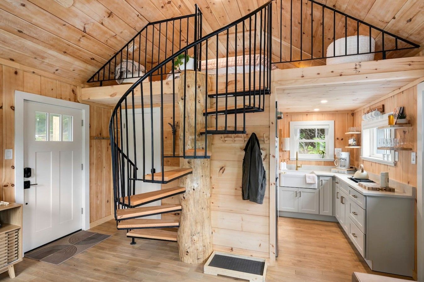 A wooden interior with a spiral staircase, a kitchen area, and a door.