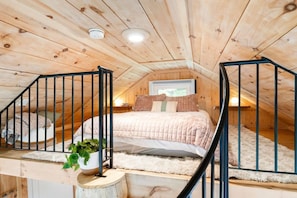 A cozy attic bedroom with a bed, a potted plant, and a staircase.