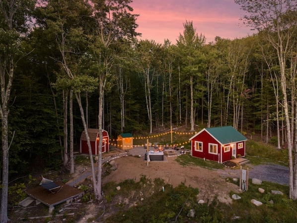 A cabin surrounded by trees with a fire pit and string lights.