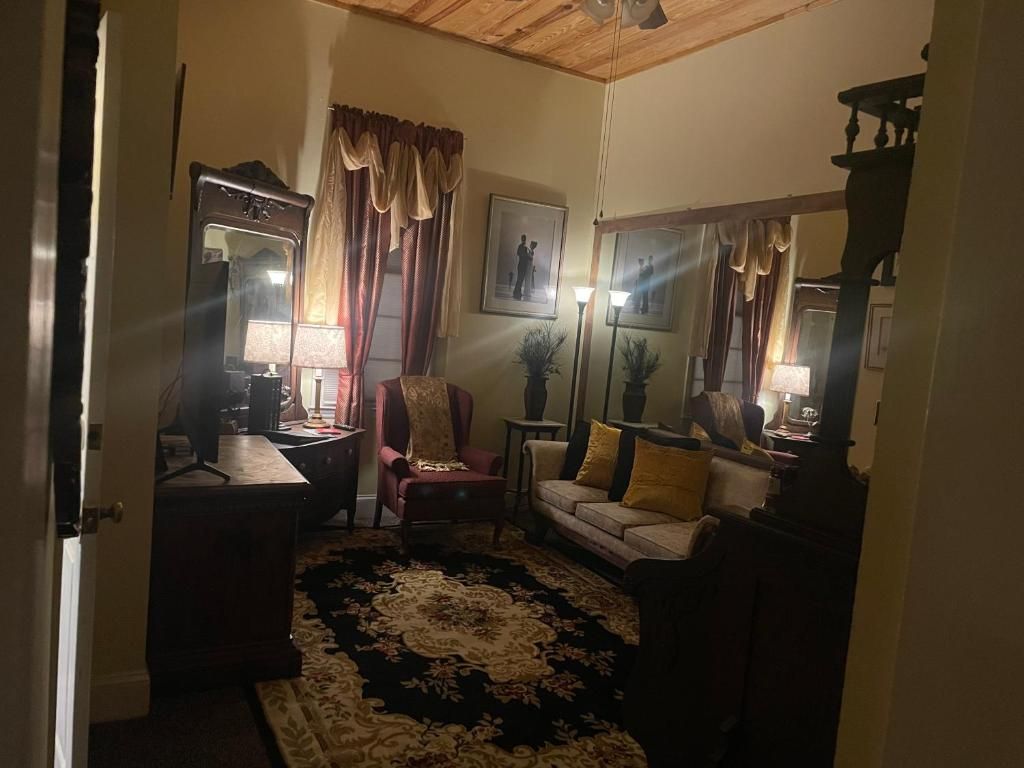 A room with a wooden ceiling, a sofa, a chair, a small table, a lamp, a mirror, and a framed picture on the wall.