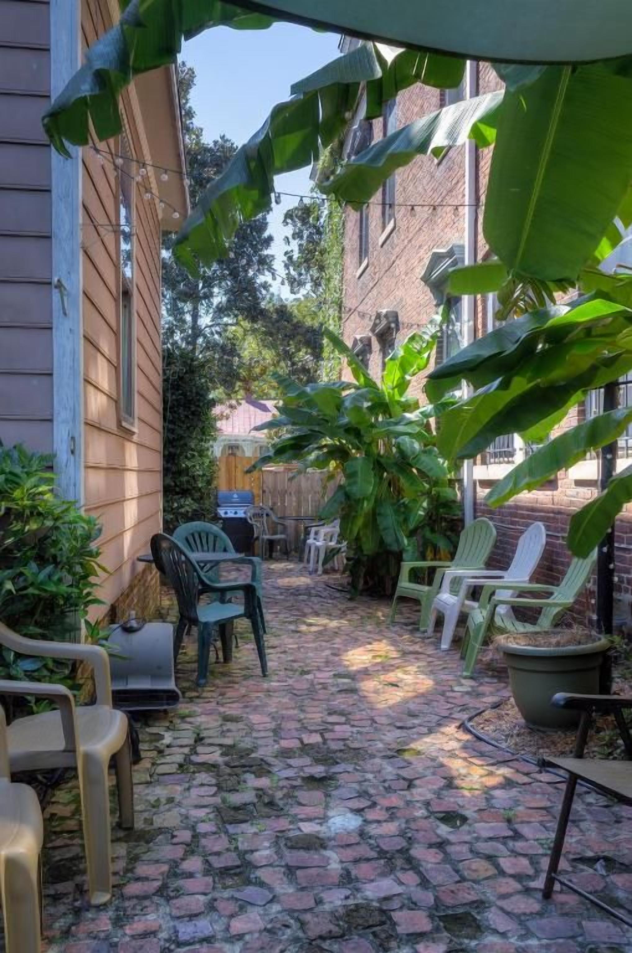 A narrow brick pathway with outdoor furniture and potted plants.