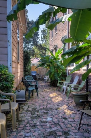 A narrow brick pathway with outdoor furniture and potted plants.