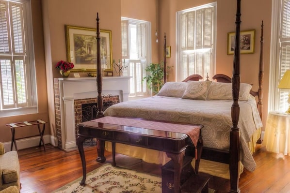 A traditional bedroom with a four-poster bed, a fireplace, and a large window with shutters.