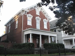 A two-story brick building with a porch and a small fence in front.
