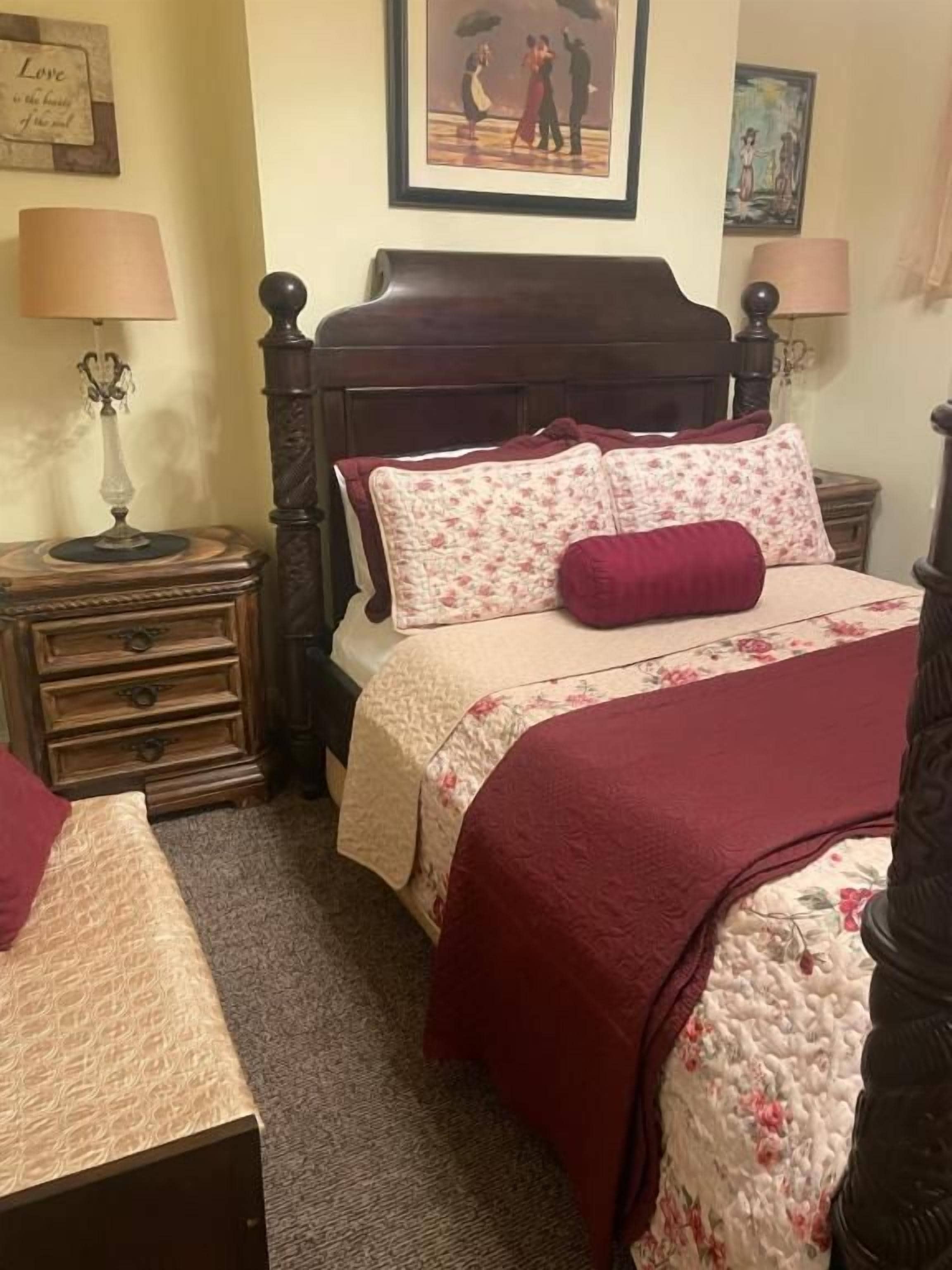 A bedroom with a wooden bed, two bedside tables, a nightstand, and a wall-mounted lamp.