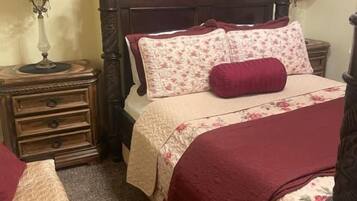 A bedroom with a wooden bed, two bedside tables, a nightstand, and a wall-mounted lamp.