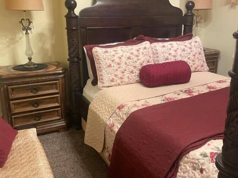A bedroom with a wooden bed, two bedside tables, a nightstand, and a wall-mounted lamp.
