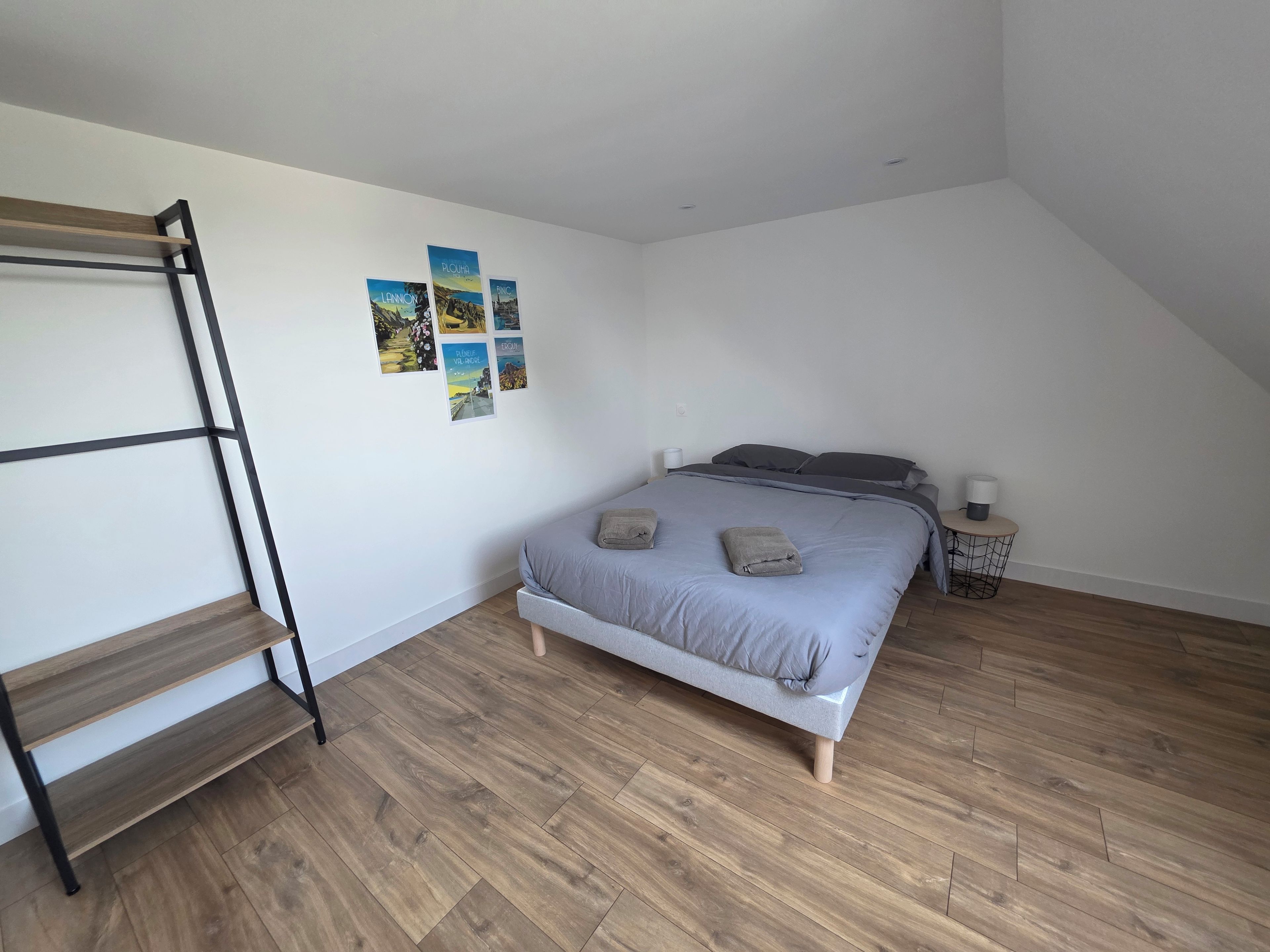 Une chambre avec un lit superposé, une table de chevet, une lampe et une étagère fixée au mur.