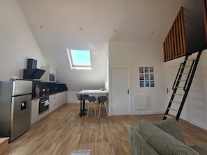 A compact living space with a kitchenette, a dining area, and a loft bedroom with a skylight.