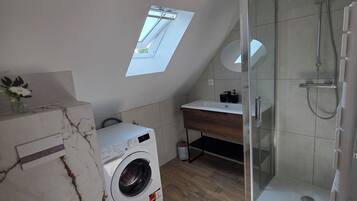 Une salle de bain moderne dotée d’un puits de lumière, d’un lave-linge, de toilettes et d’une douche à parois de verre.