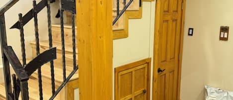 A wooden staircase with a wrought iron railing, a wooden door, and a stone floor.