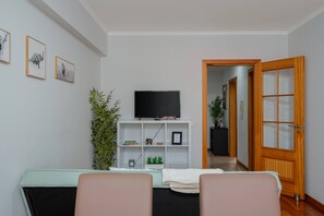 A living room with a flat-screen TV on a white shelf, a door with glass panels, and a potted plant. - Simon's Apartment by Galmi (Machico)