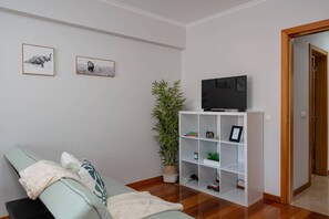 A living room with a sofa, a television on a stand, a bookshelf, and two framed pictures on the wall. - Simon's Apartment by Galmi (Machico)