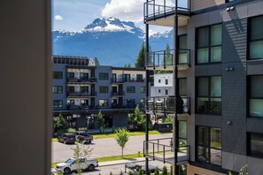 A multi-story building with balconies, a parking area, and a view of snow-capped mountains. - Revelhaus (Revelstoke)