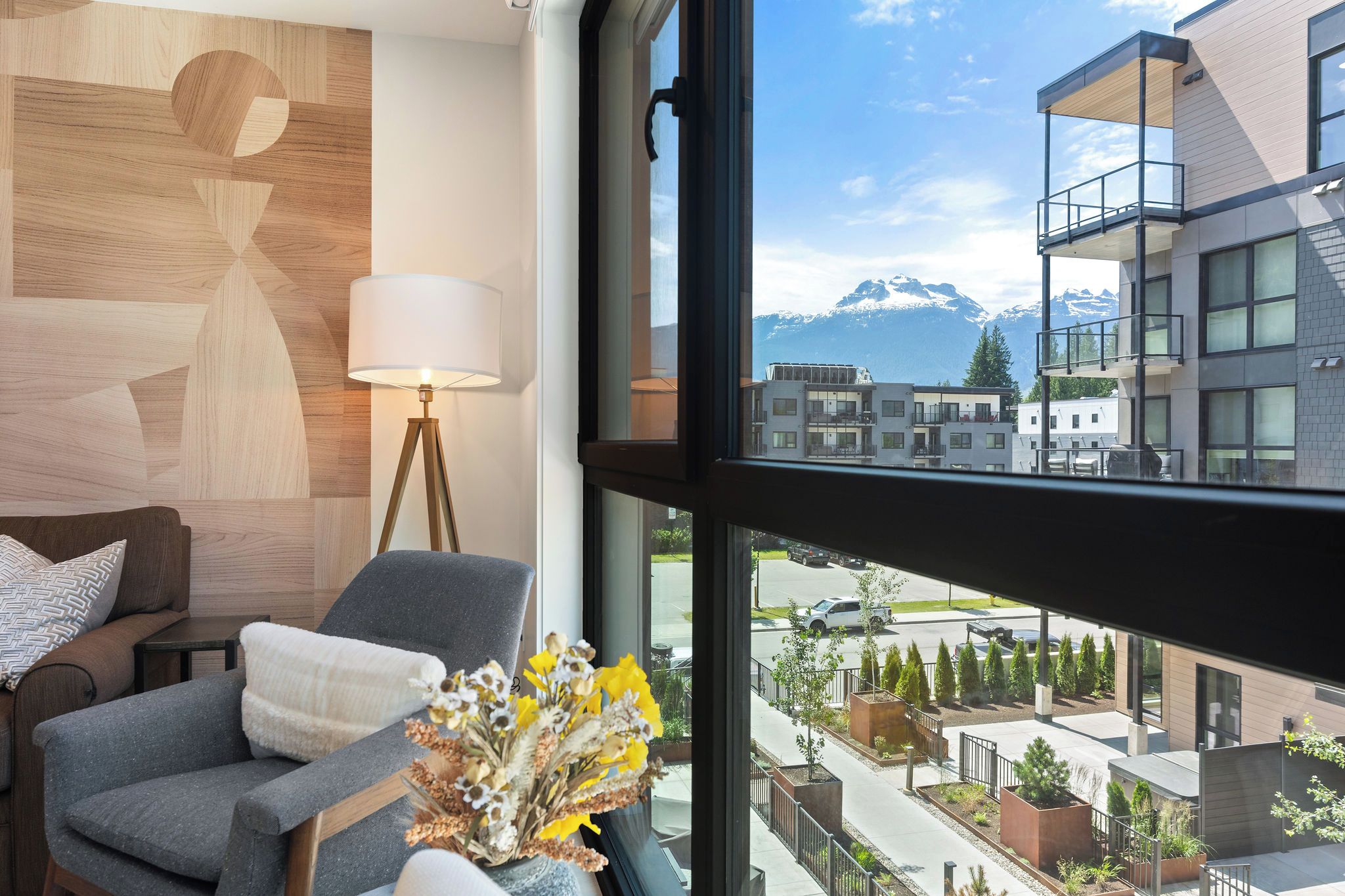 A modern hotel room with a view of a mountain range, a sofa, a lamp, and a vase with flowers.