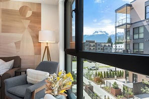 A modern hotel room with a view of a mountain range, a sofa, a lamp, and a vase with flowers. - Revelhaus (Revelstoke)