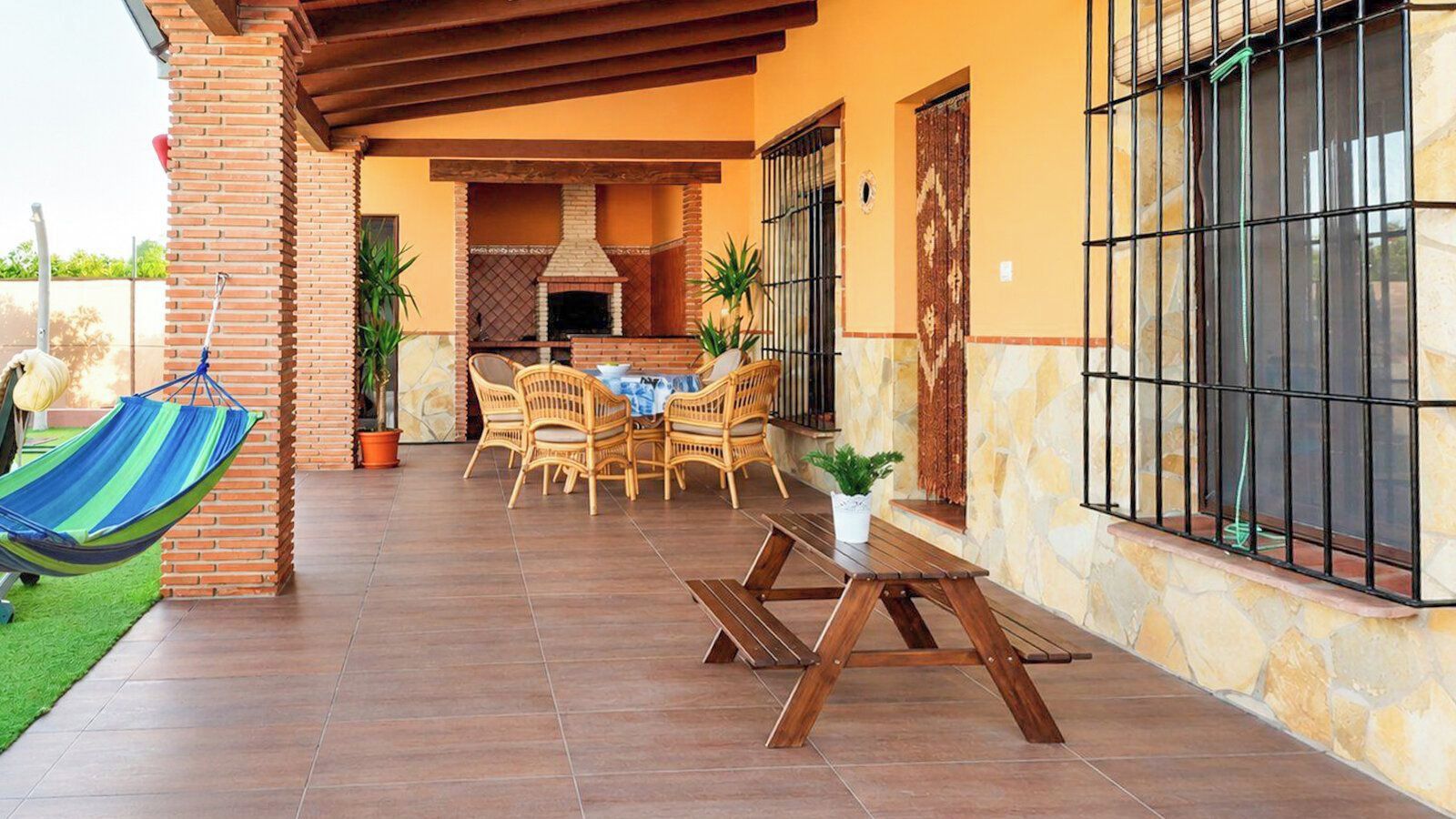 An outdoor patio with a brick fireplace, wicker furniture, and a hammock.
