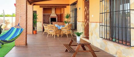 Un patio al aire libre con chimenea de ladrillo, muebles de mimbre y una hamaca.