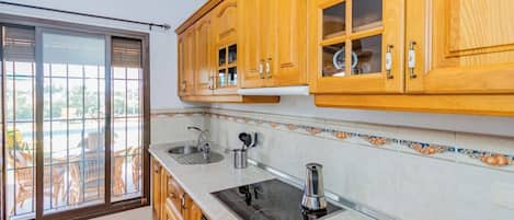 Une cuisine avec des meubles en bois, un évier en acier inoxydable et une plaque de cuisson noire.