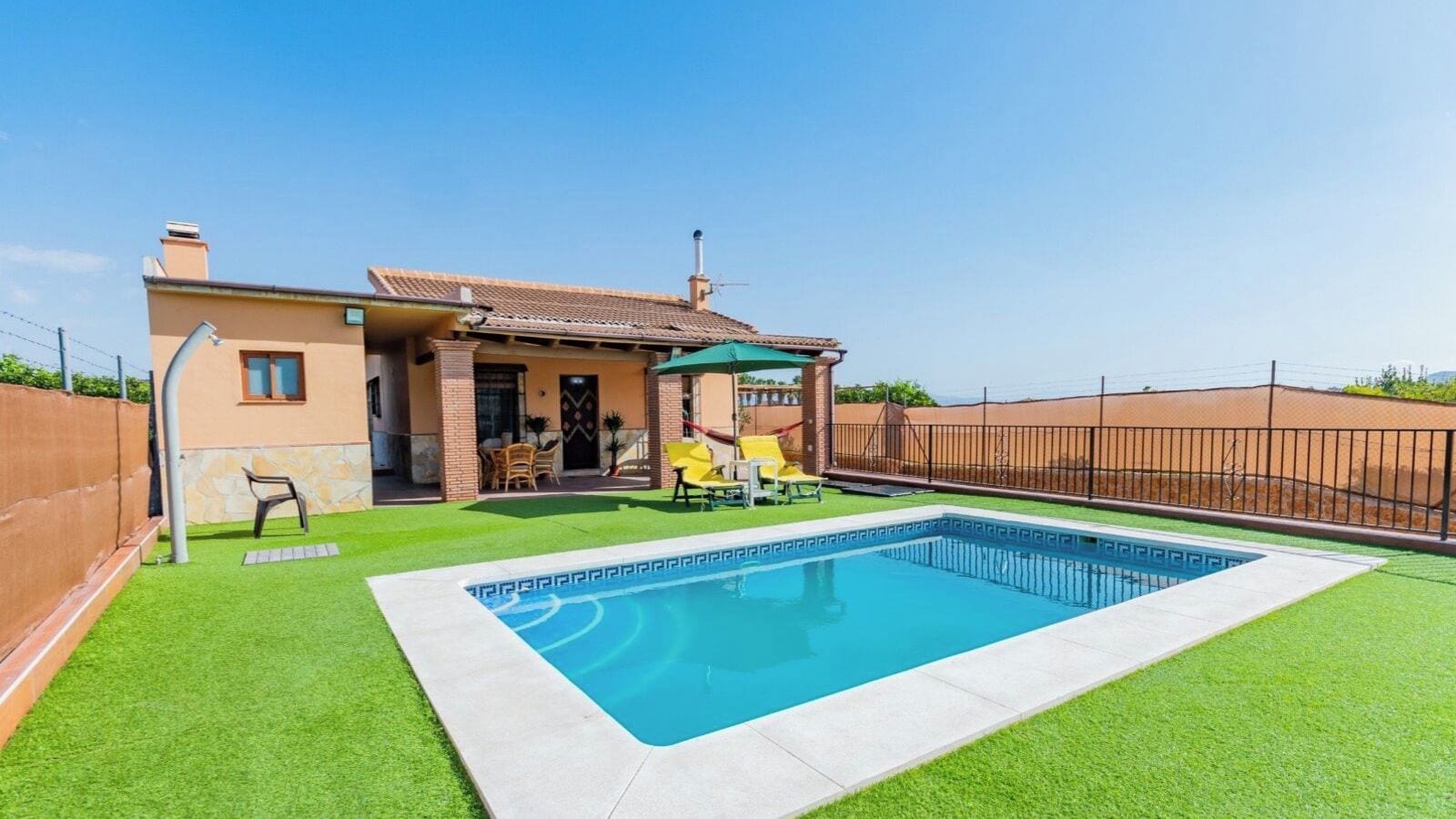 A residential property with a swimming pool, a covered patio, and a fenced backyard.