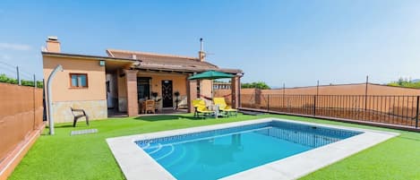 A residential property with a swimming pool, a covered patio, and a fenced backyard.