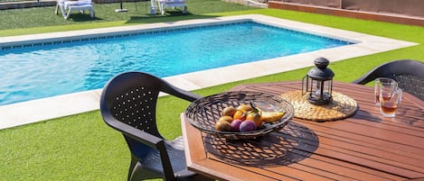 Un espace aménagé au bord de la piscine avec une table, des chaises et un panier de fruits.