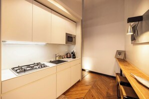 A modern kitchen with white cabinets, a gas stove, a microwave, and a wooden floor. - PoVenti5 | Art House Torino city center · PoVenti5 | Casa d'arte Torino centro (Torino)