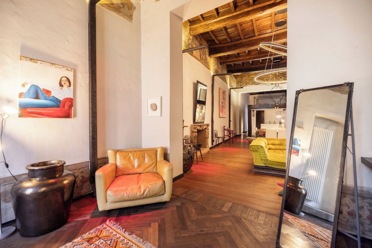 Una stanza con pavimento in legno, un divano in pelle, una poltrona rossa, uno specchio grande e un quadro appeso al muro.