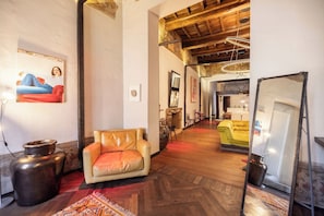 A room with a wooden floor, a leather sofa, a red armchair, a large mirror, and a painting on the wall. - PoVenti5 | Art House Torino city center · PoVenti5 | Casa d'arte Torino centro (Torino)