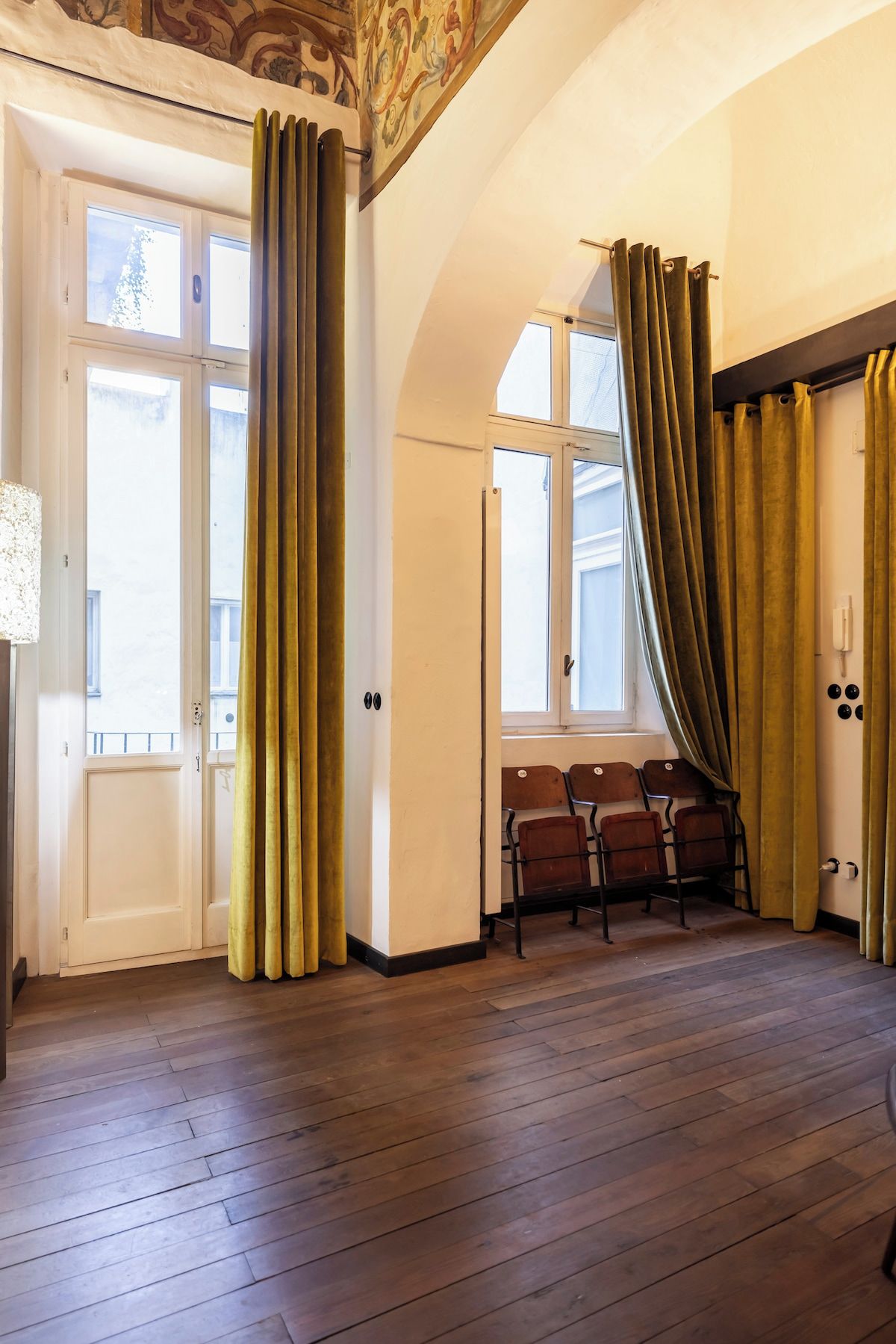 A room with wooden flooring, a seating area with chairs, and a window with curtains.