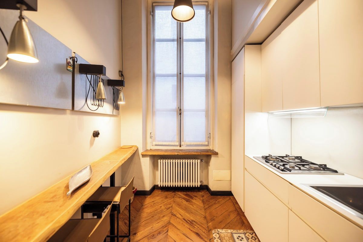 Eine kompakte Küche mit Fischgrätparkett, einem Fenster mit Aussicht, einem Gasherd und Pendelleuchten.