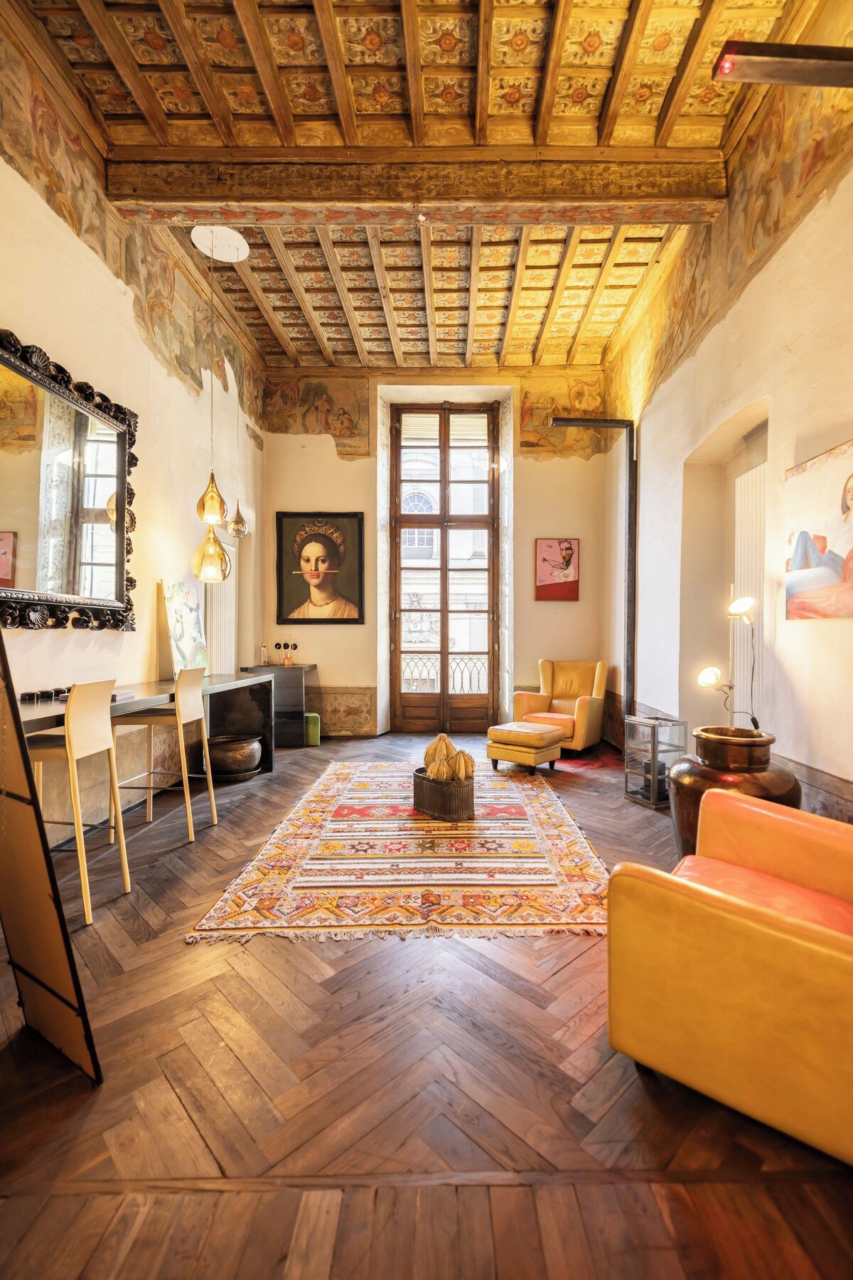 Una stanza con pavimento in parquet a spina di pesce, un'ampia finestra, un divano, una poltrona e un tavolo con uno specchio.