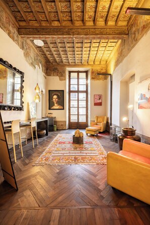 A room with a wooden herringbone floor, a large window, a sofa, a chair, and a table with a mirror. - PoVenti5 | Art House Torino city center · PoVenti5 | Casa d'arte Torino centro (Torino)