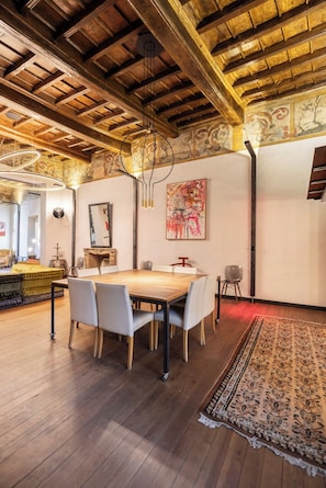 A dining area with a wooden table and chairs, a patterned rug, and a ceiling with exposed beams and decorative moldings. - PoVenti5 | Art House Torino city center · PoVenti5 | Casa d'arte Torino centro (Torino)