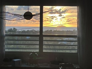 A window with a view of a sunset over a landscape, including a body of water and distant land. - Beautiful 3-bedroom house with ocean view and amazing sunsets in charming Rincon (Rincon)