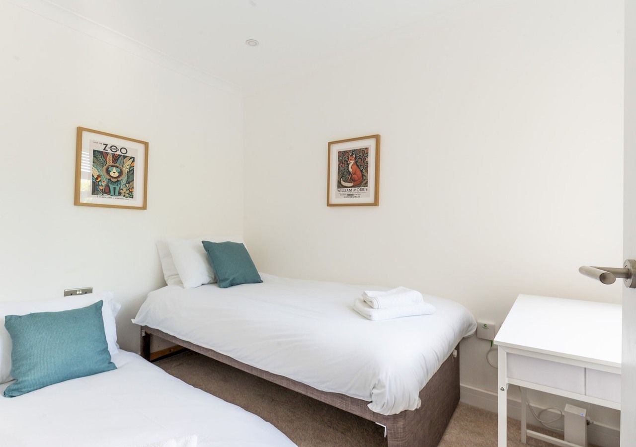 Una habitación de hotel con dos camas individuales, una mesita de noche blanca y un escritorio pequeño con una silla.
