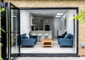 Ein modernes Wohnzimmer mit zwei Sofas und einem Couchtisch, im Hintergrund eine Küche und eine Glastür, die nach draußen führt.