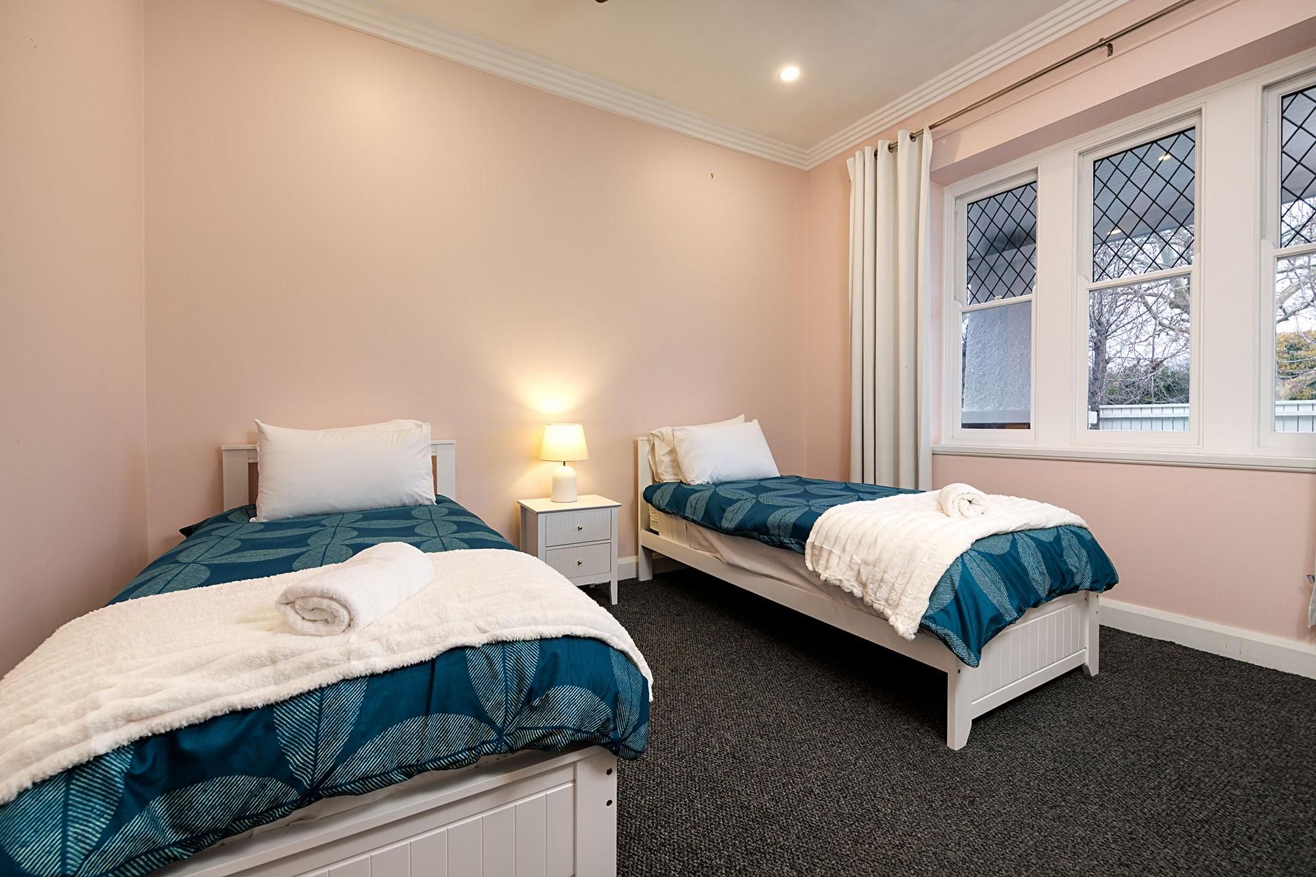 A twin room with two beds, a nightstand, a lamp, and a window with a view.