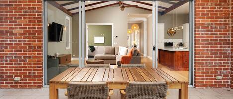 Ein Holztisch mit zwei Korbstühlen vor einer Glastür, die in ein Wohnzimmer mit einem Sofa und einem Couchtisch führt.