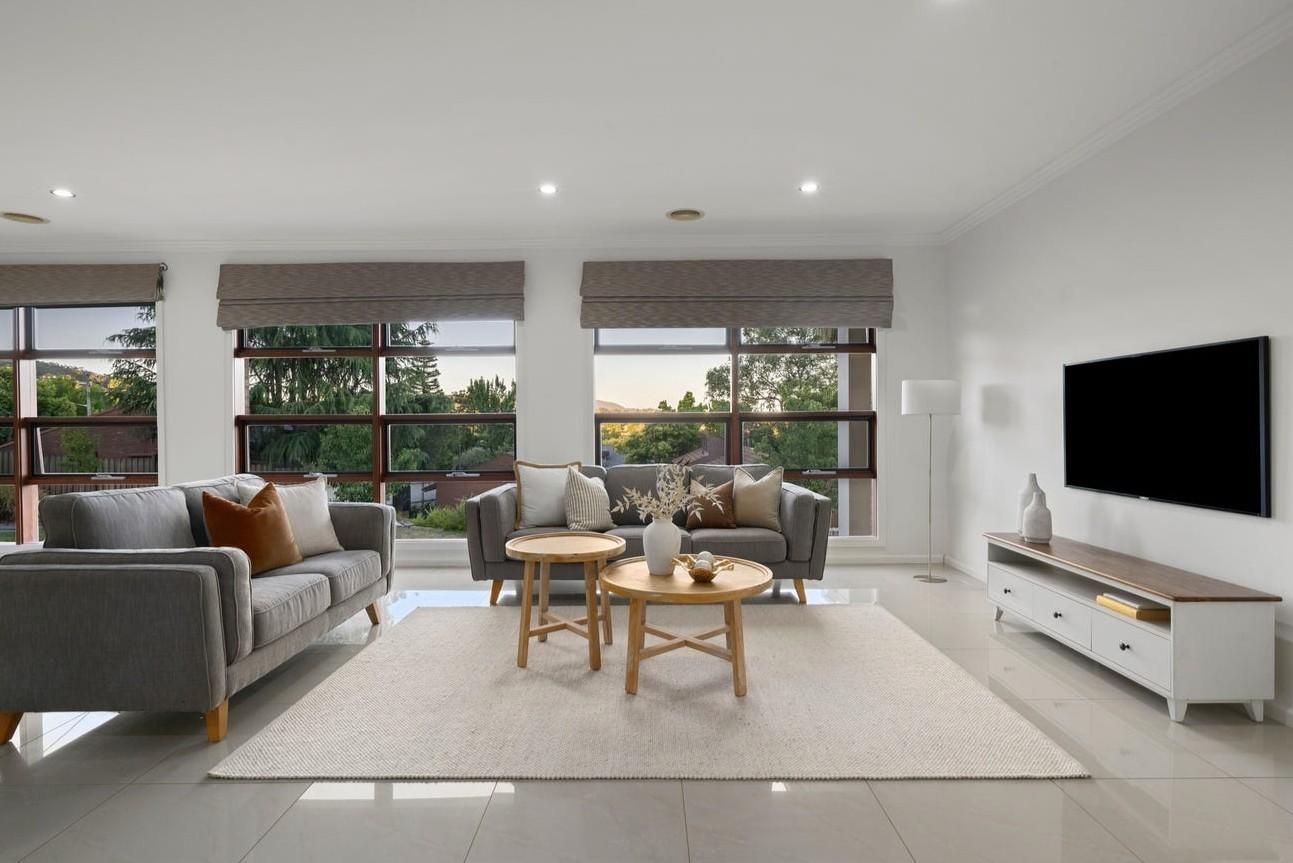 A modern living room with a sofa, two round wooden tables, and a flat-screen TV.