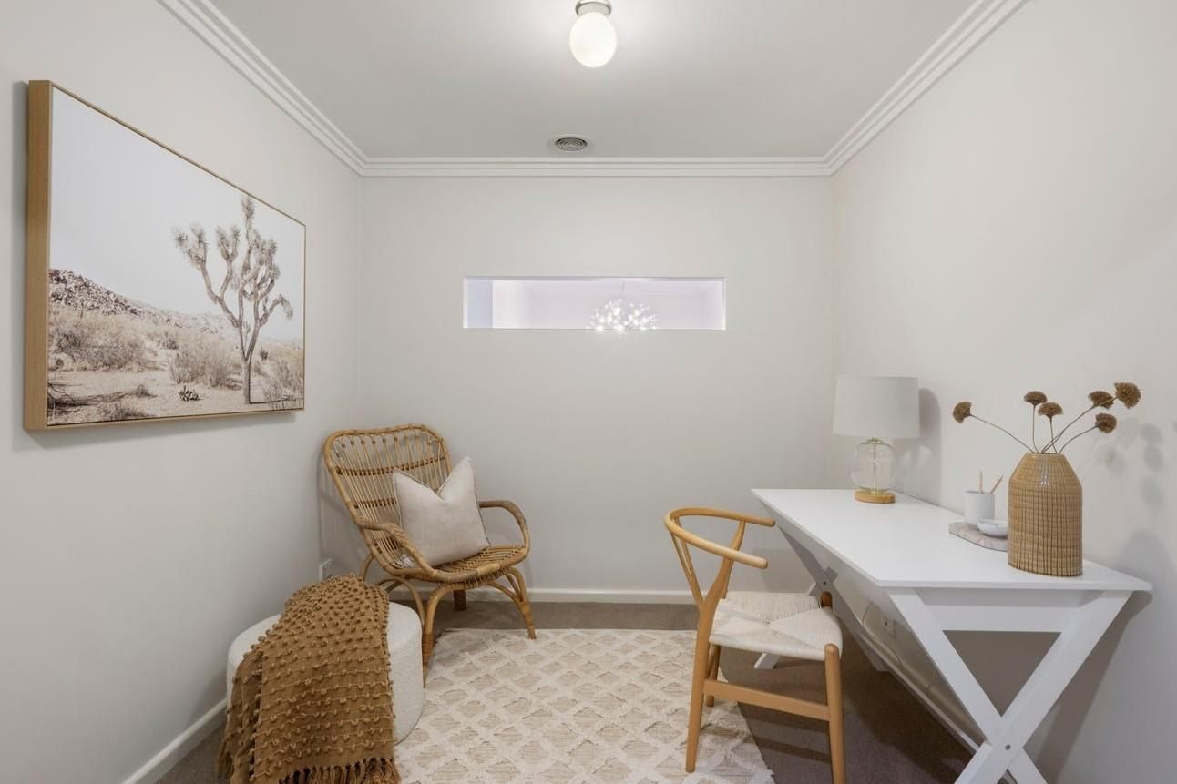 A room with a white desk, two chairs, a small window, a wall-mounted picture, and a ceiling light.