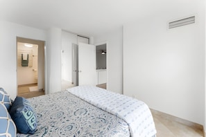 A bedroom with a bed, a bedside table, a wardrobe, and a bathroom visible through an open door. - Kihei, Kauhale Makai, Spacious 4 BR, Beachfront, Sleeps 12 (Kihei)