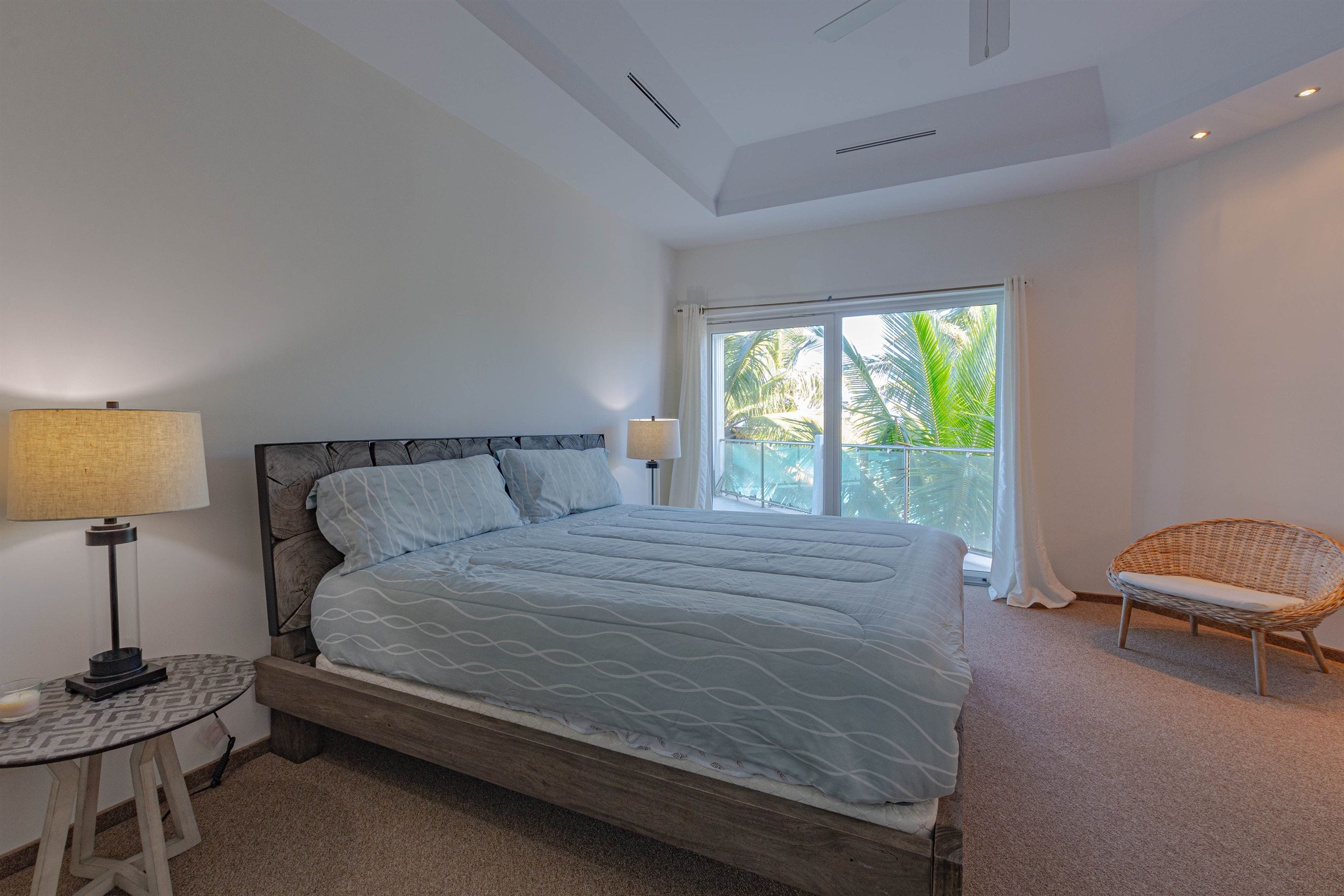 Un dormitorio con cama, una silla, una mesita de noche y una ventana con vista a palmeras.